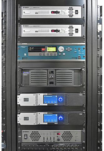 最適な環境を維持するアンプ室に整然と並ぶ機器架群。写真左＝「SHURE」の4chワイヤレス受信機「ULXD4Q」、「ヤマハ」のI/Oラック「Rio1608-D2」、さまざまな入出力がスムーズに行なえるよう考えられたパッチ盤などが収納されたラック。写真中＝デジタルマルチプロセッサー「MRX7-D」、「AFC3」システムおよび残響付加プロセッサー「LAP3-AFC」、メインスピーカーを駆動する「NEXO NXAMP4×2　MK2」パワーアンプが収納されたラック。写真右＝サラウンドスピーカー用のパワーアンプ「ヤマハPX8」